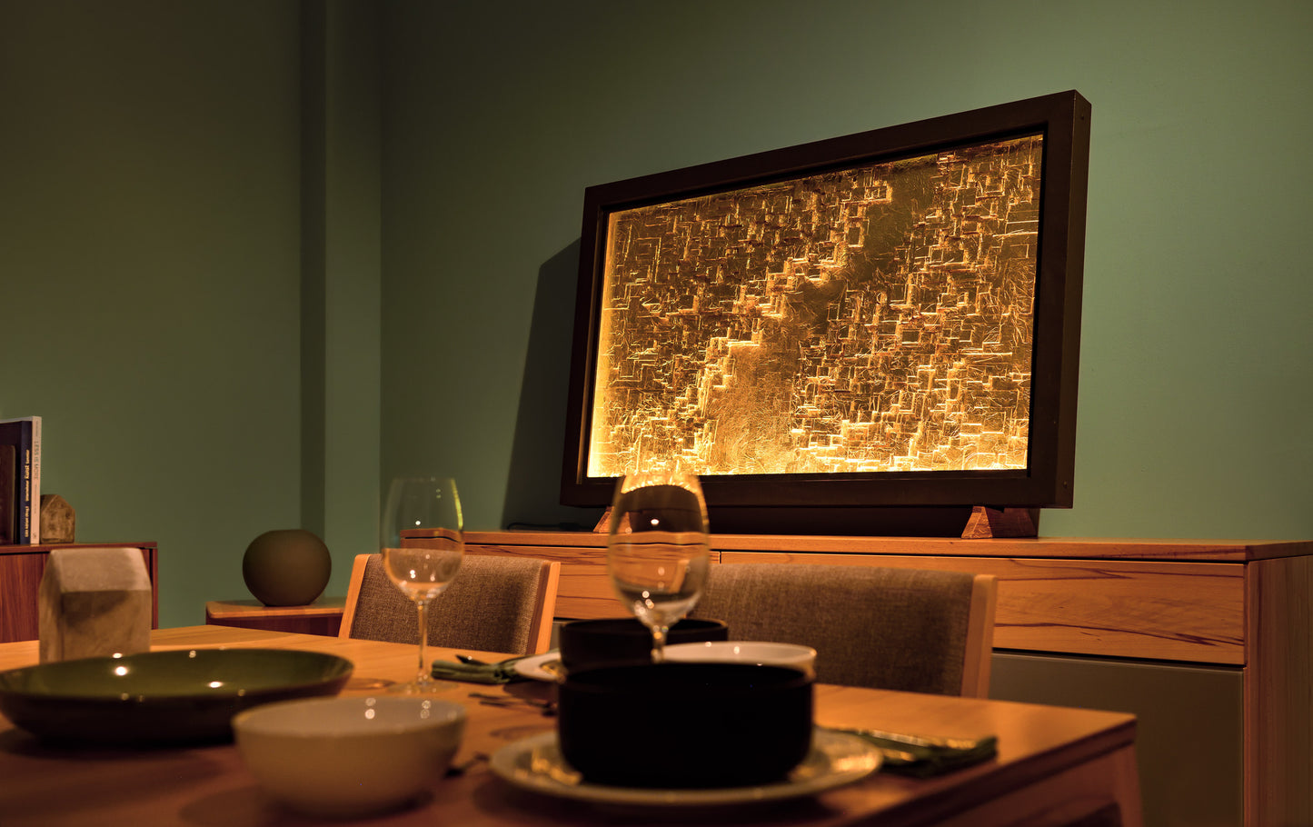 Große, eingerahmte Ambienteleuchte mit goldenen Strukturen auf einem Sideboard neben einem Esstisch in Wohnlicher Atmosphäre