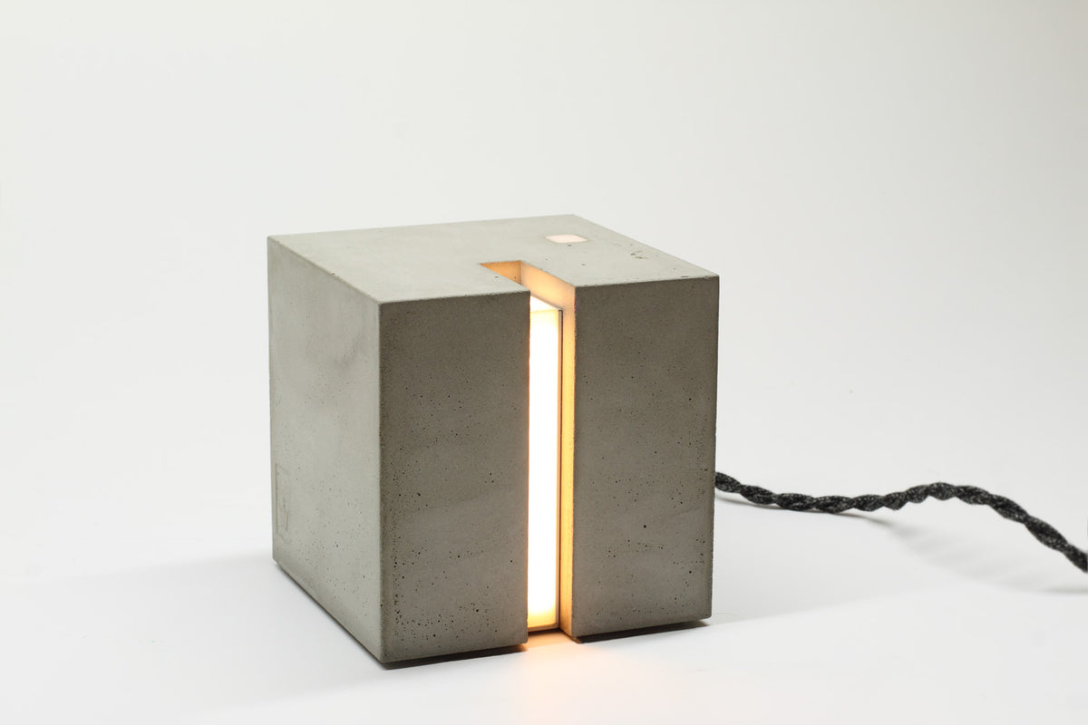 Eine hellgraue Beton Leuchte in form eines Würfels auf einem Tisch.